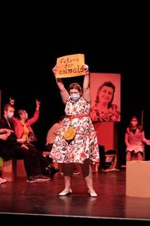 Person in Blumenkleid hält Schild "Future for animals", andere sitzen im Hintergrund.