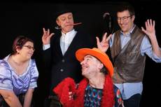 Vier Personen in bunten Kostümen, eine mit Löffel im Mund.