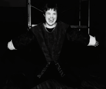 Person in mittelalterlichem Kostüm, lächelnd mit ausgebreiteten Armen.